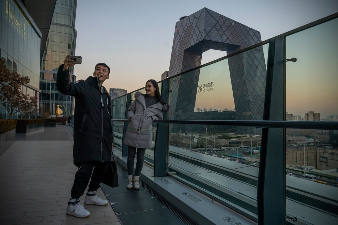 People take a selfie, with the China Central Television Tower as background, in Beijing on  December 13, 2021. China assets are predicted to offer investors stability this year. Photo: Bloomberg