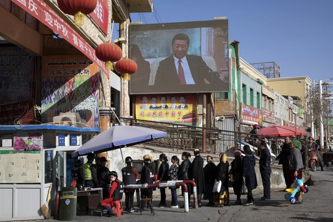 Residents line up at a security checkpoint into the bazaar in Hotan, Xinjiang, where a screen shows Chinese President Xi Jinping. Photo: AP