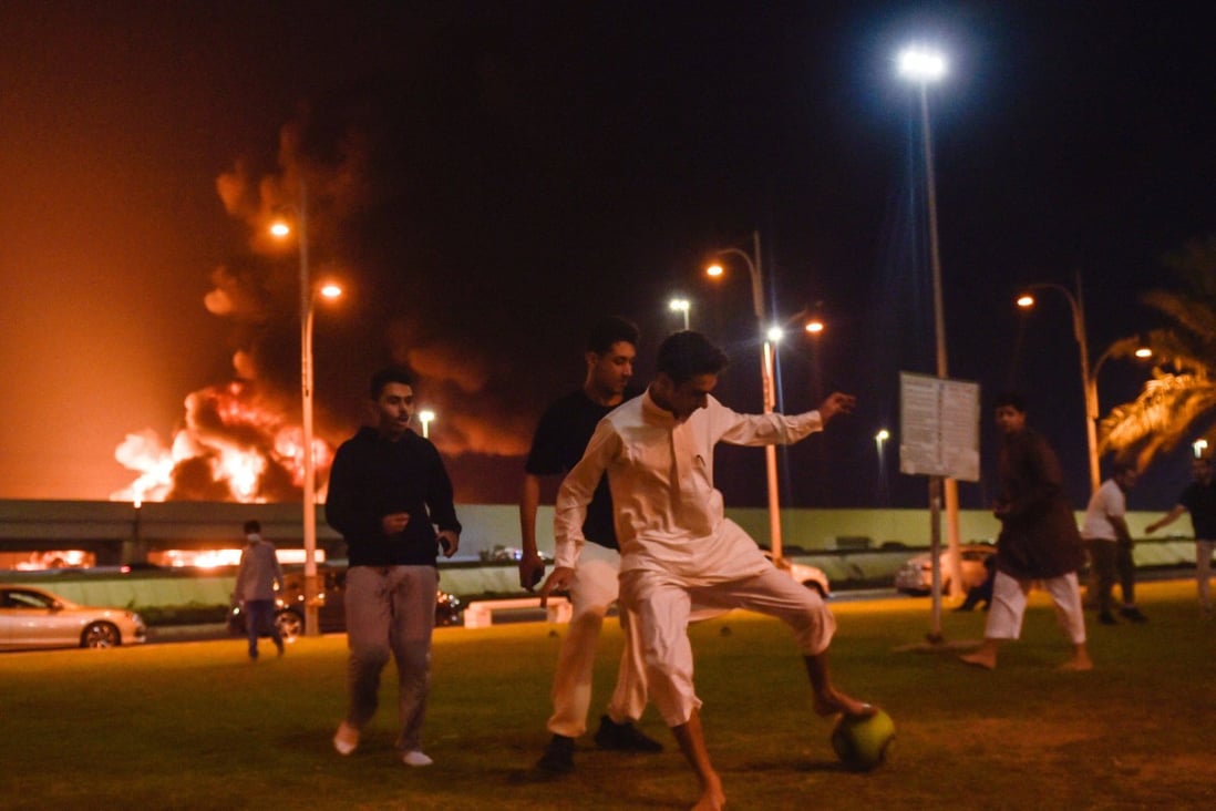 Youngsters in Jeddah play football as smoke and flames rise from a Saudi Aramco oil facility in the distance behind them. Photo: AFP