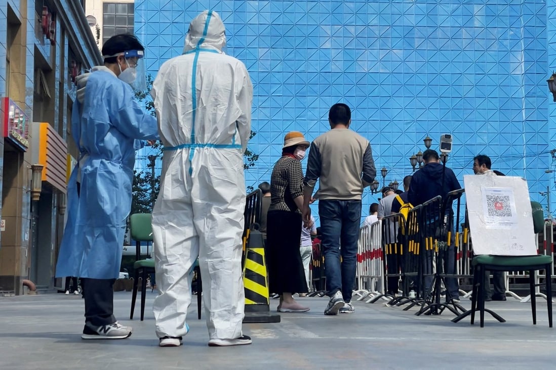 Workers in protective suits stand next to people lining up a makeshift nucleic acid testing site during a mass testing clinic in Chaoyang district of Beijing on May 4, 2022. Photo: Reuters