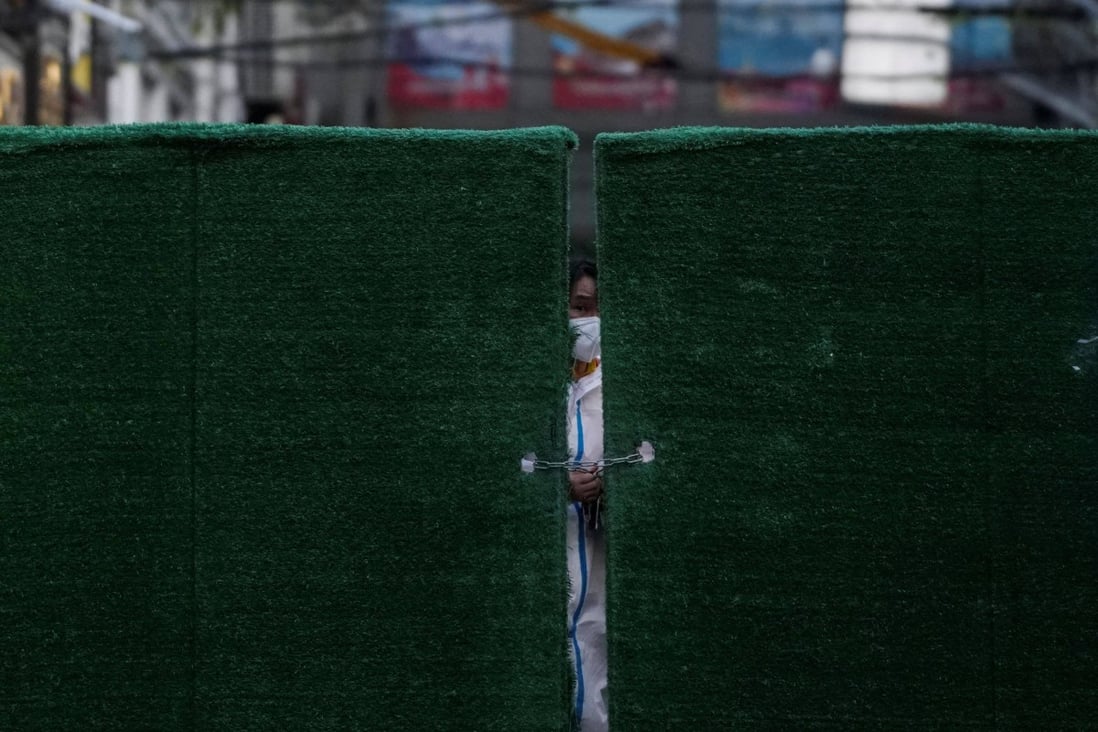 A worker in a protective suit locks a barrier outside of a residential complex in Shanghai, China. Photo: Reuters