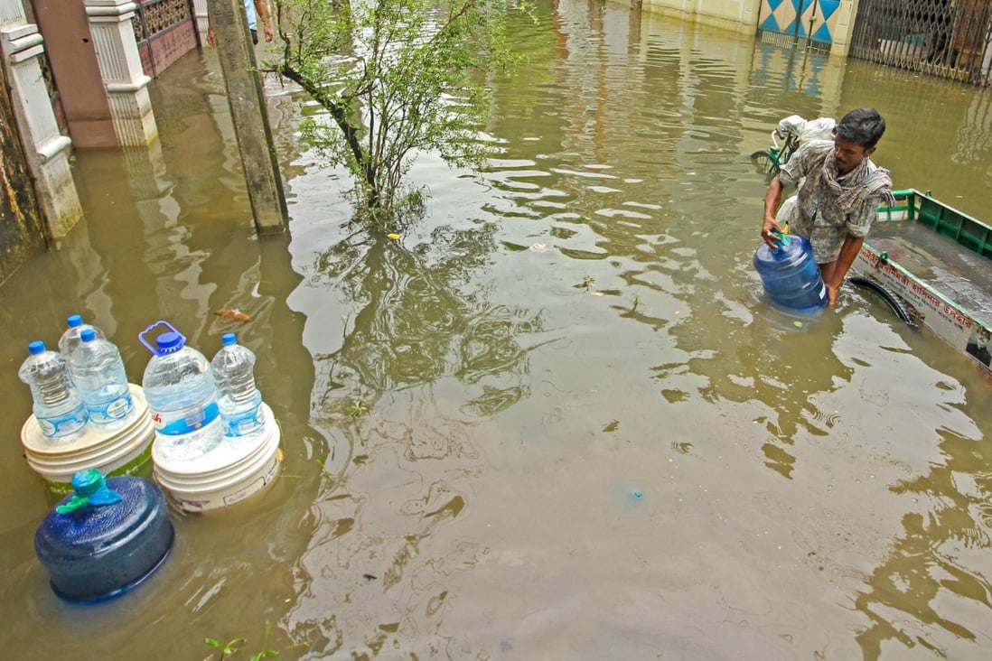 A man delivers drinking water to houses along a flooded street following heavy rains in Sylhet, Bangladesh. Photo: AFP