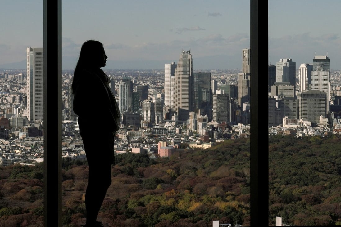 A woman stands in front of a view of autumn leaves and Shinjuku skyscrapers in Tokyo on November 29, 2019. Photo: EPA-EFE