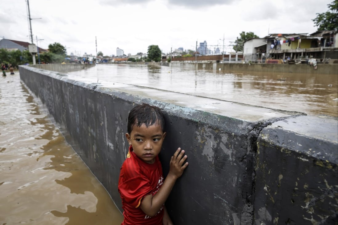 A boy stands next to a wall along a flooded road in Jakarta, Indonesia, in 2020. Amid climate change, governments should track environmental health risks to children. Photo: EPA-EFE