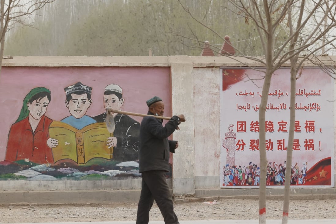 A farmer walks past murals and posters depicting ethnic minority residents studying the constitution with slogans reading “Unity and stability is fortune, separatism and turmoil is misfortune” near Kashgar, Xinjiang, on March 19, 2021. Photo: AP