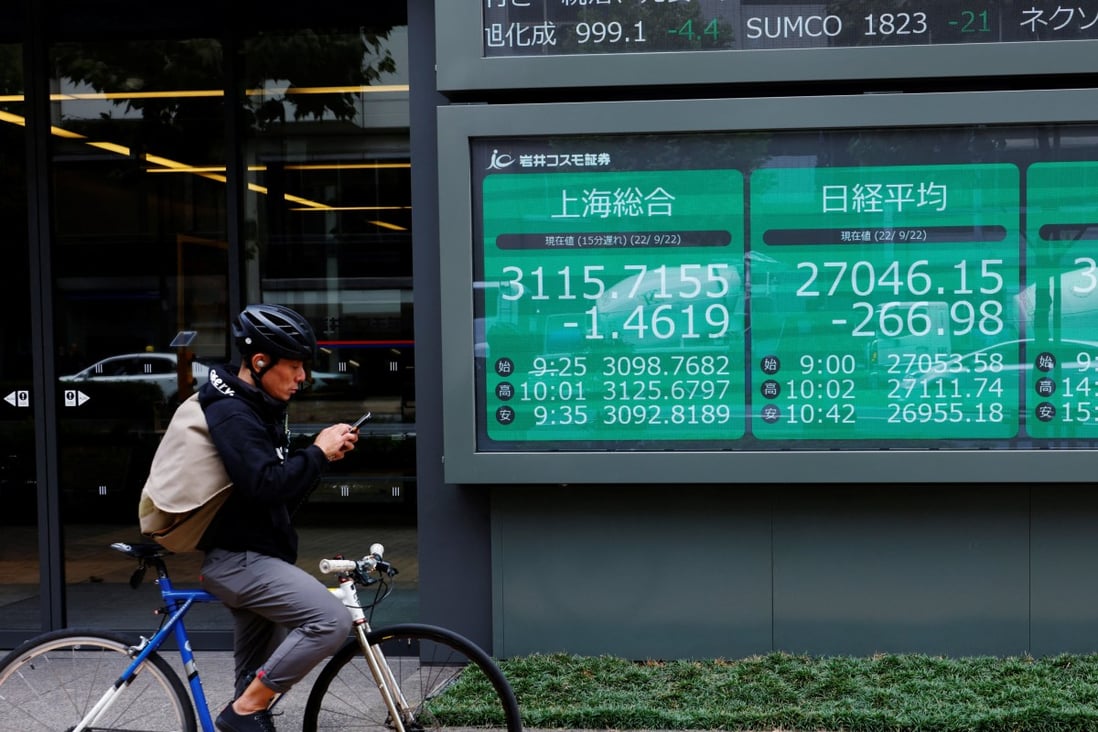 A cyclist looking at his phone near an electronic board in Tokyo showing stock prices on Shanghai stock exchange. Photo: Reuters
