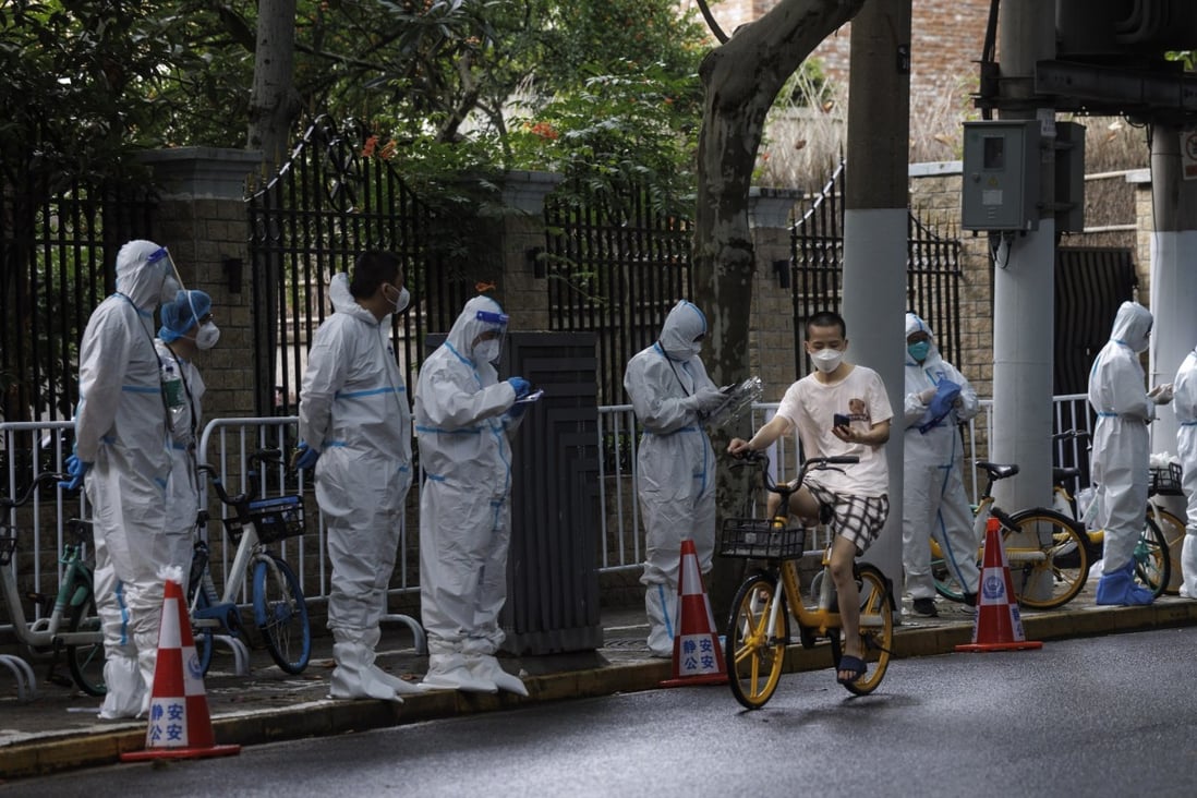 A man on a bicycle past workers in protective gear amid a new round of lockdowns in Shanghai on 4 June 2022. Photo: EPA-EFE