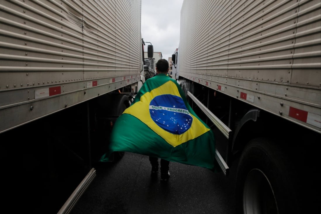 A supporter of President Jair Bolsonaro with a Brazilian flag walks between trucks during a blockade on Castelo Branco highway, on the outskirts of Sao Paulo, Brazil. Photo: AFP