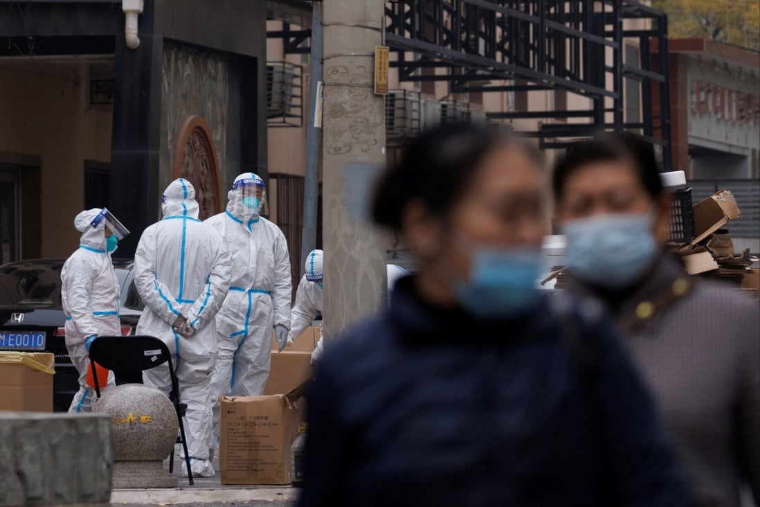 In Beijing on November 18, residents walk near pandemic prevention workers in protective suits in a locked-down residential compound as coronavirus outbreaks continue in China’s capital. Photo: Reuters
