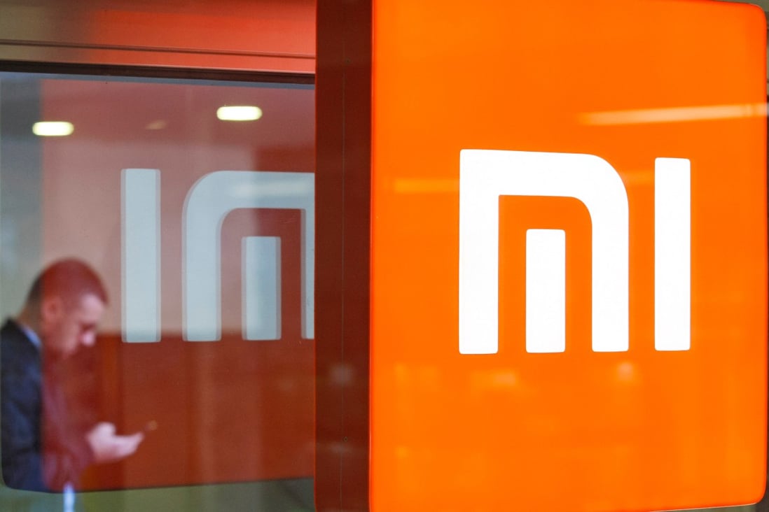 A man looks at his smartphone next to a reflected Xiaomi logo. Photo: Shutterstock