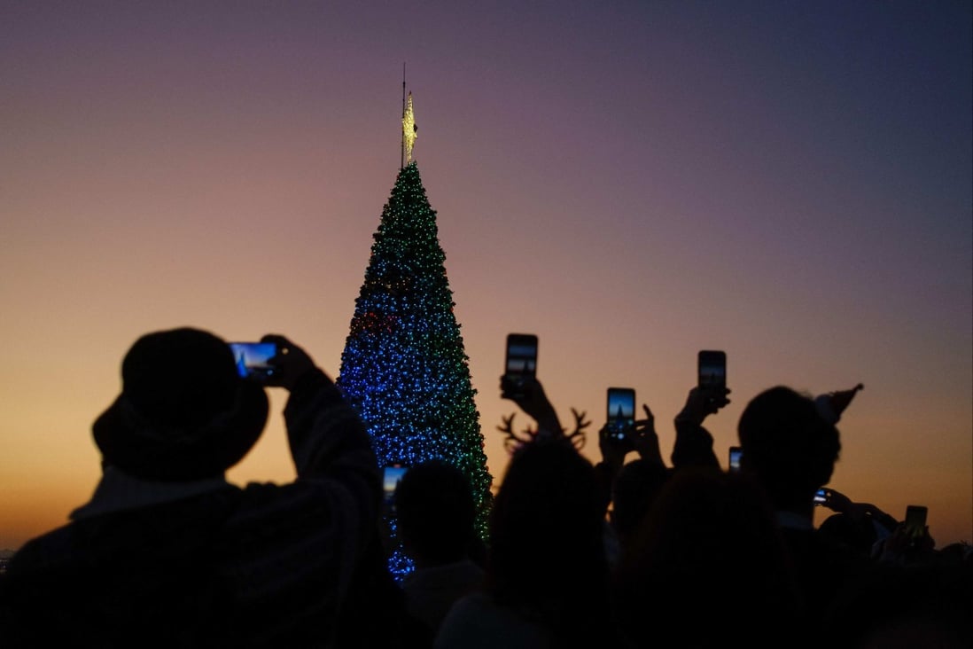 People take photos of a Christmas tree by the waterfront in the West Kowloon district in Hong Kong on December 25. As we welcome a new year full of possibilities, Hong Kong must learn from the hiccups that other countries have experienced in reopening. Photo: AFP