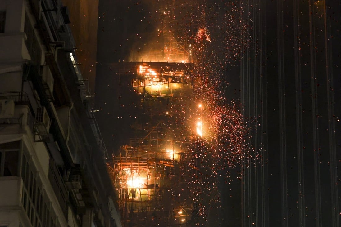 A high-rise apartment building in Hong Kong is engulfed in flames with sparks and falling debris, highlighting urban high-rise vulnerabilities amid a catastrophe.