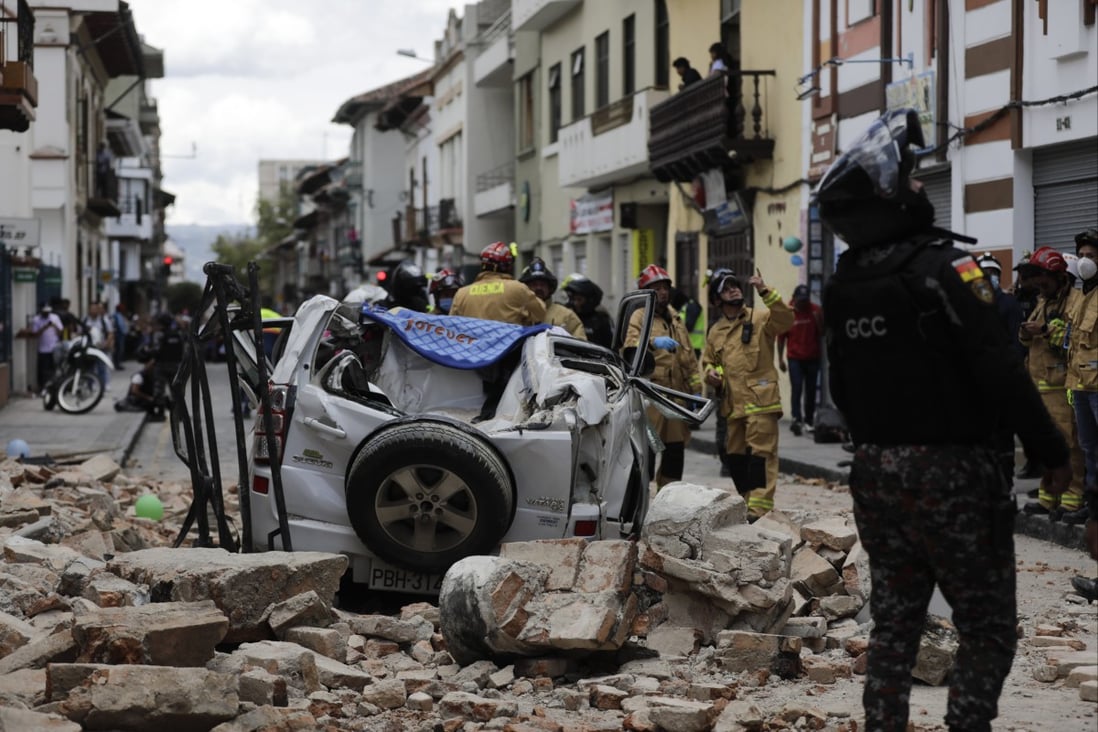 A police officer looks up next to a car crushed by debris after an earthquake shook Cuenca, Ecuador on Saturday. Photo: AP