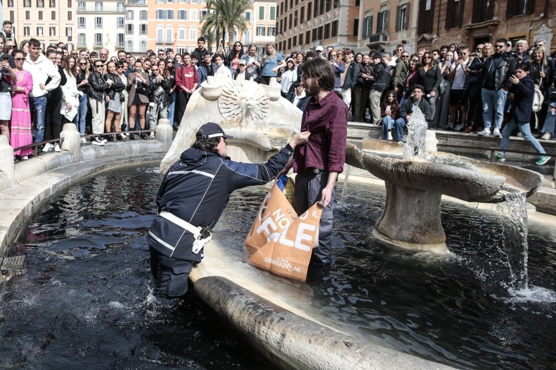 A police officer removes an environmental activist standing in the fountain of Barcaccia in front of Rome’s Spanish Steps with black paint and a banner against fossil fuel. Photo: LaPresse via Zuma Press / dpa