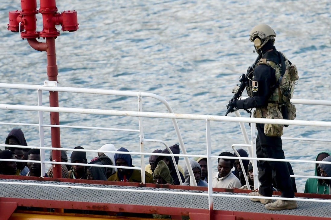 An armed policeman stands guard over migrants from the El Hiblu 1 tanker in Valletta's Grand Harbour on Thursday. Photo: AFP