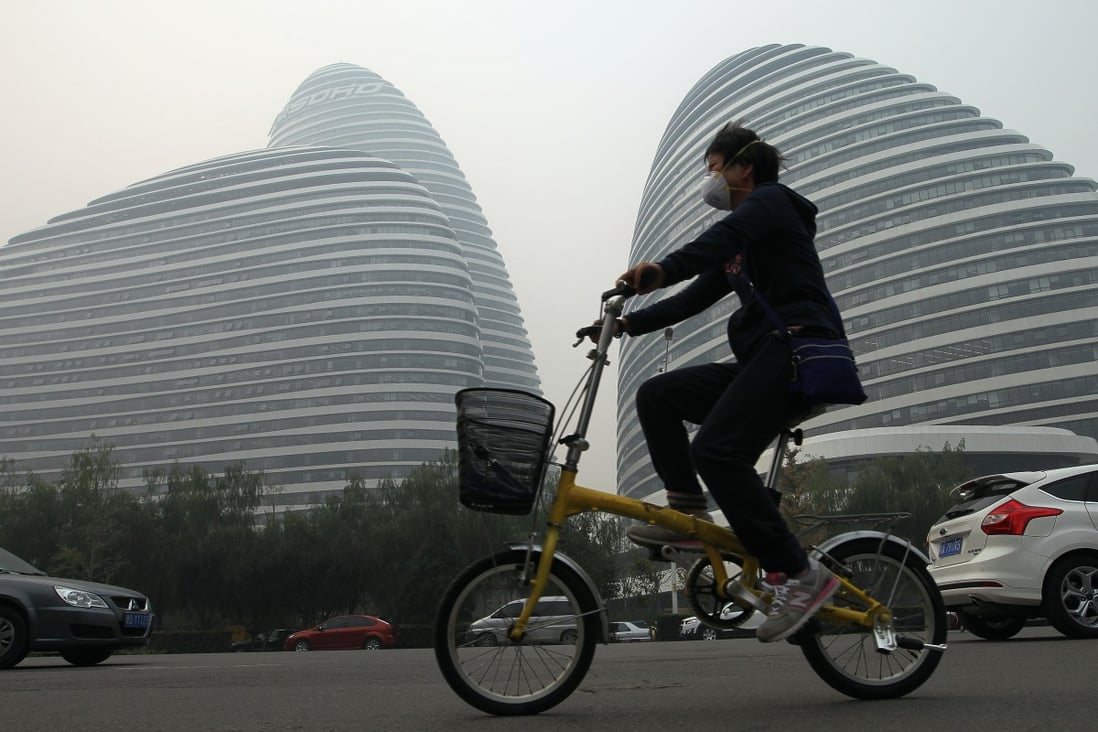 A woman wearing mask rides a bike passing by the Wangjing SOHO office towers in Beijing on October 9, 2014. The office towers, designed by Iraqi-British architect Zaha Hadid, is one of the biggest cash cows for their developer Soho China. Photo: SCMP/Simon Song