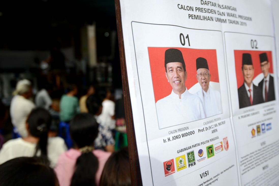 Indonesians wait next to a poster of presidential candidates at a polling centre. Photo: AFP