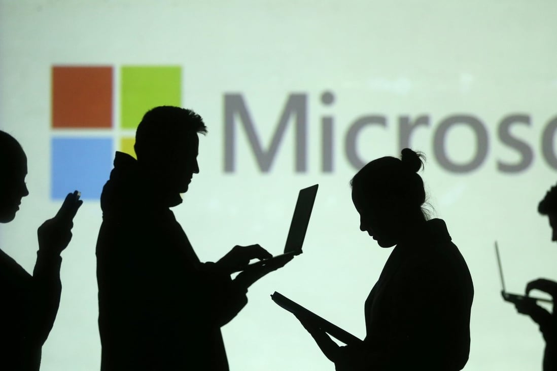 Silhouettes of laptop and mobile device users are seen next to a screen projection of Microsoft logo in this picture illustration taken March 28, 2018. Photo: Reuters