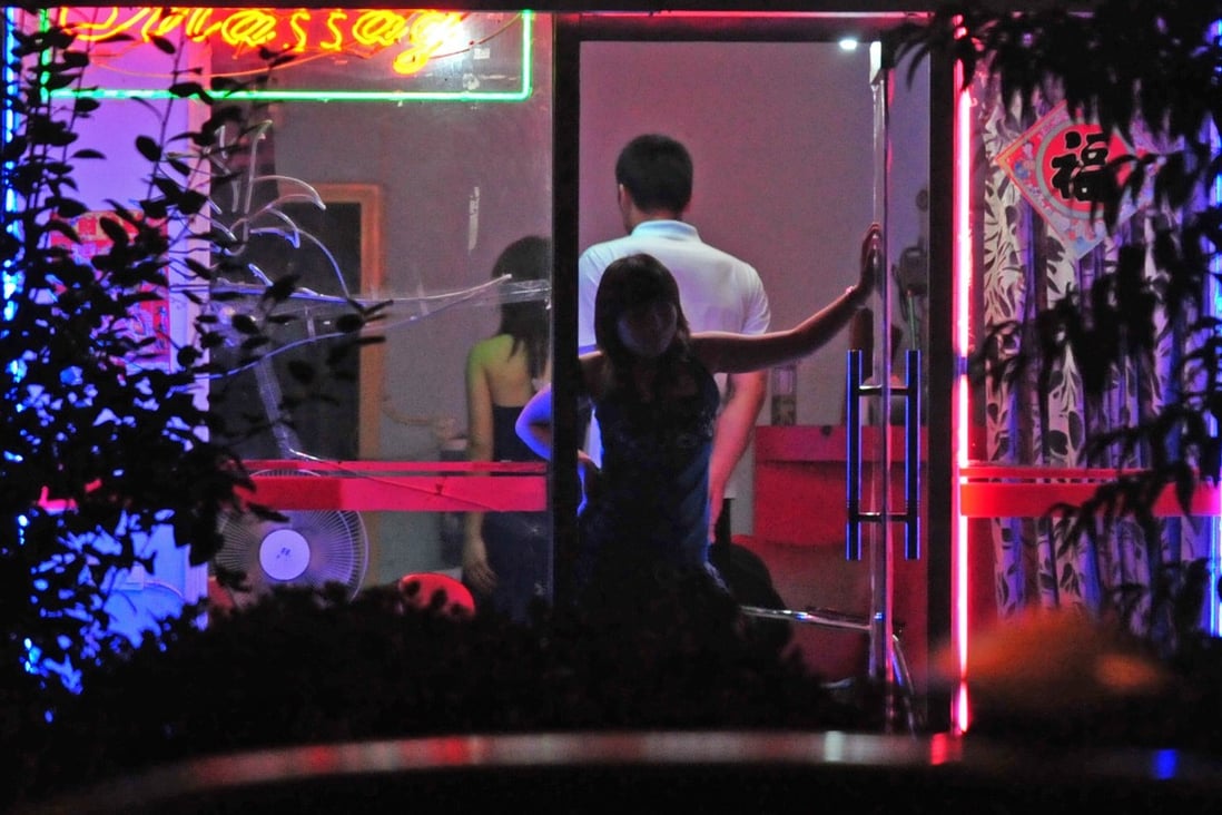 A woman stands in the doorway of a neon-lit “barber shop” in Beijing in July 2008. Some sex workers operate from stores like these, which have nothing to do with haircuts. Photo: AFP