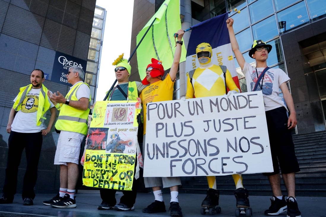 Protesters, some of them claiming to have been seriously injured during the last six months Yellow Vest demonstrations, hold a placard reading in French “Join our forces for a more just world”. Photo: AFP