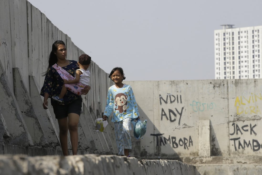 People walk near part of sea wall which prevents water flooding Jakarta. Photo: AP