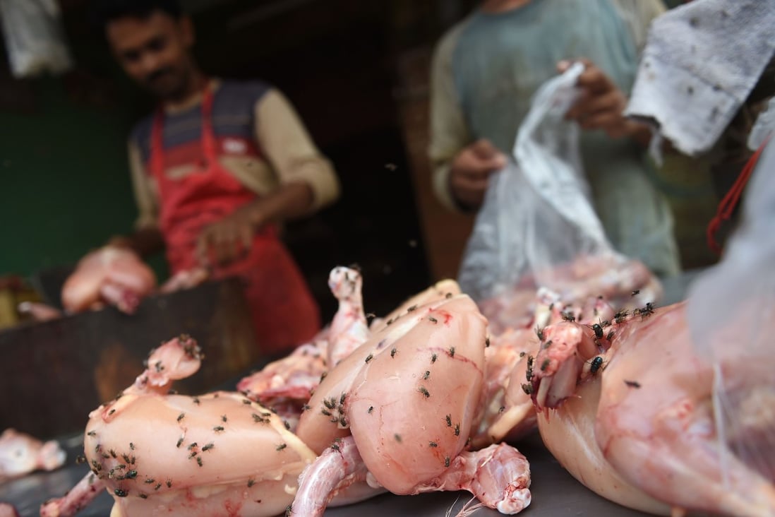 A butcher cuts up chicken as flies sit on the meat in a market in Karachi. Photo: AFP