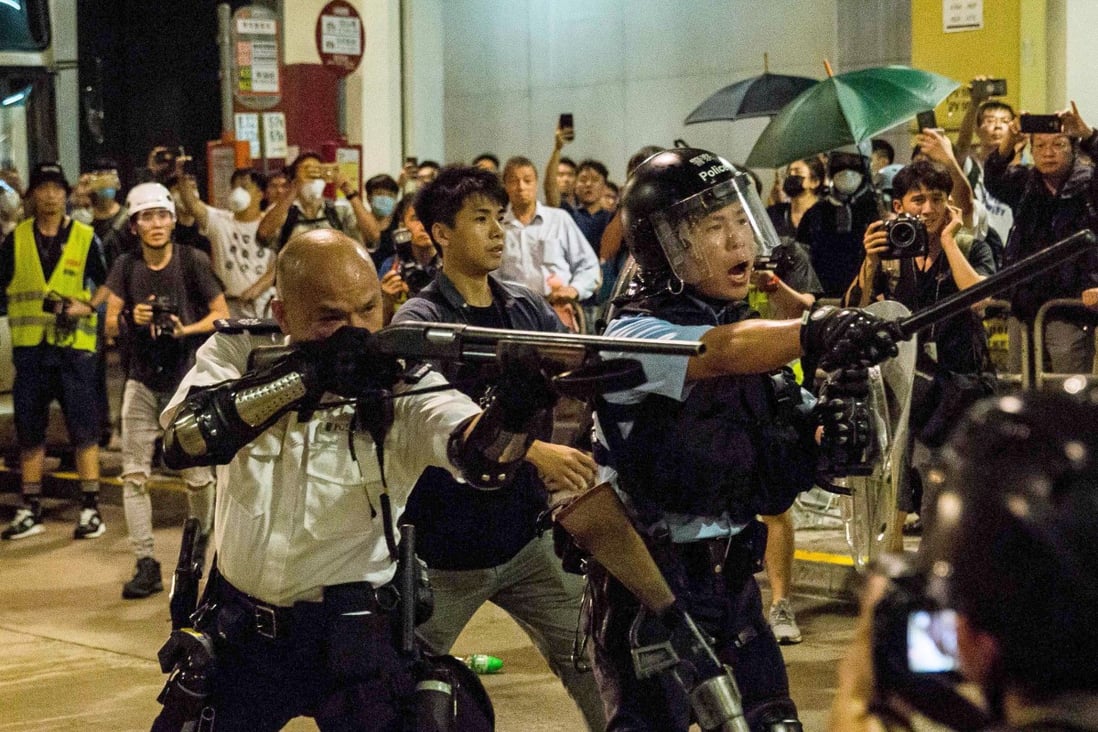 Sergeant Lau Chak-kei points his shotgun at protesters who had gathered outside Kwai Chung Police Station. Photo: AFP