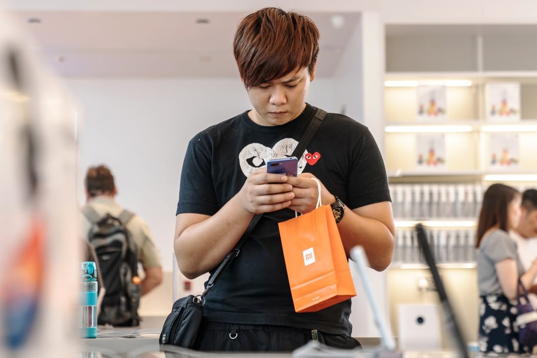 A customer holding a Xiaomi Corp-branded shopping bag uses a smartphone inside a Xiaomi store in Hong Kong on July 6, 2018. Photo: Bloomberg