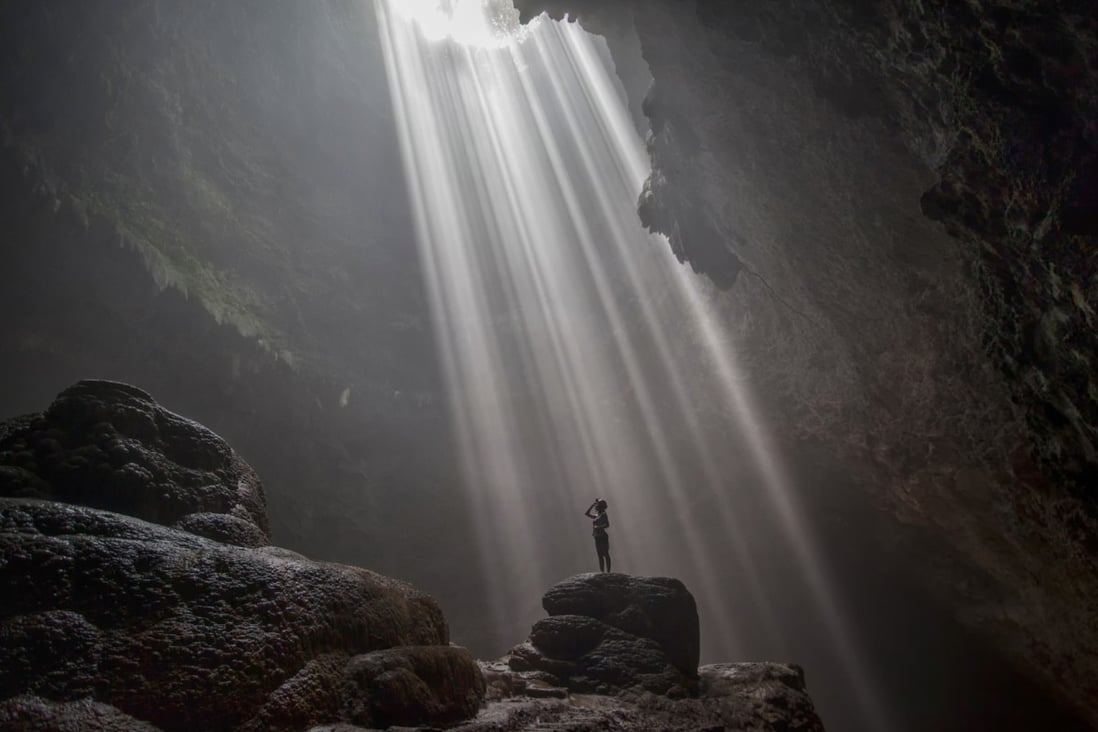 Inside Grubug cave, Indonesia, where the “light of heaven”, a beam of sunlight, shines through a hole in the roof. The cave is reached via a passageway from Jomblang cave. The caves are a growing destination for adventurous tourists in Yogyakarta province, Java. Photo: Shutterstock
