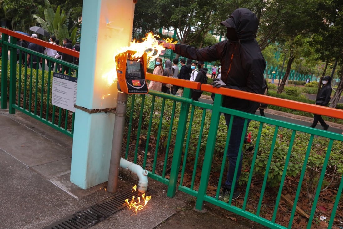 A black-clad protestor attempts to set fire to a card reader at Tin Sau Light Rail station, in Tin Shui Wai. Photo: Felix Wong