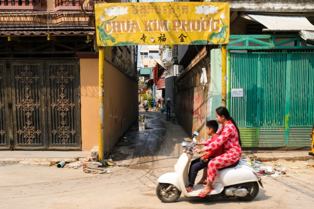 A woman and a child ride past an entrance sign, in Vietnamese and Khmer, to Kim Phuoc temple community in Chbar Ampov, Phnom Penh. Photo: Peter Ford