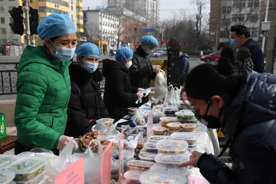 Restaurant workers in protective face masks as they sell packaged meals in a car park outside their restaurant in Beijing on February 21, 2020. Photo: AFP