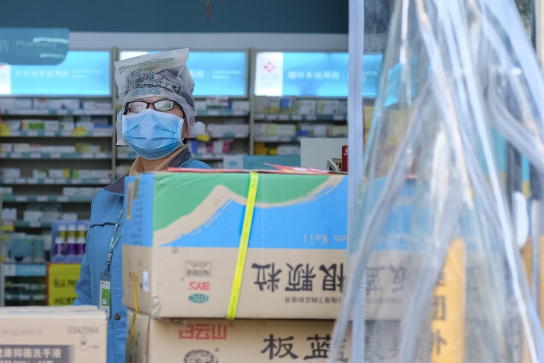 A clerk wearing a face mask and a plastic bag stands in a pharmacy in Wuhan in central China’s Hubei Province. In some provinces residents must register with their real names when purchasing fever and cough medications so that officials can follow up with them Photo: AP