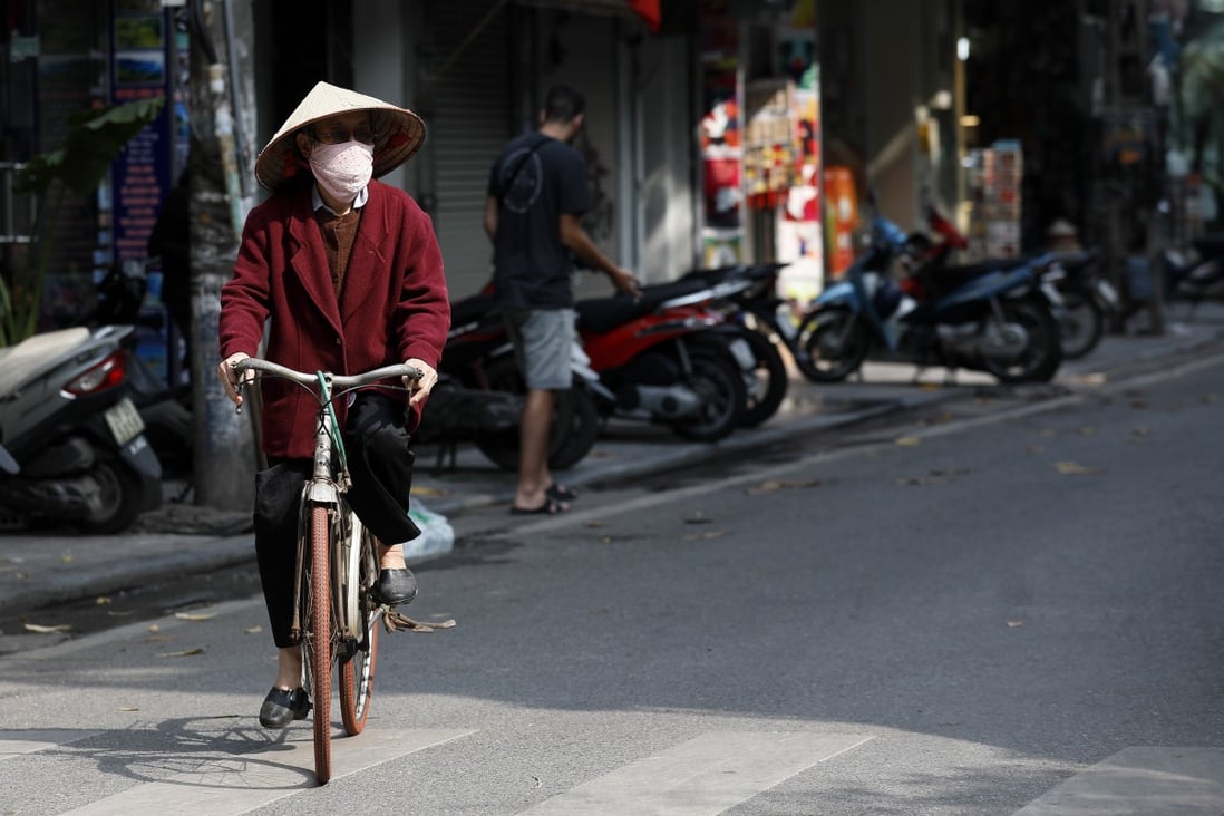 A Vietnamese woman wearing a face mask rides a bicycle in Hanoi. The capital’s streets are quiet after news of a new cluster of coronavirus infections spread. Photo: EPA-EFE