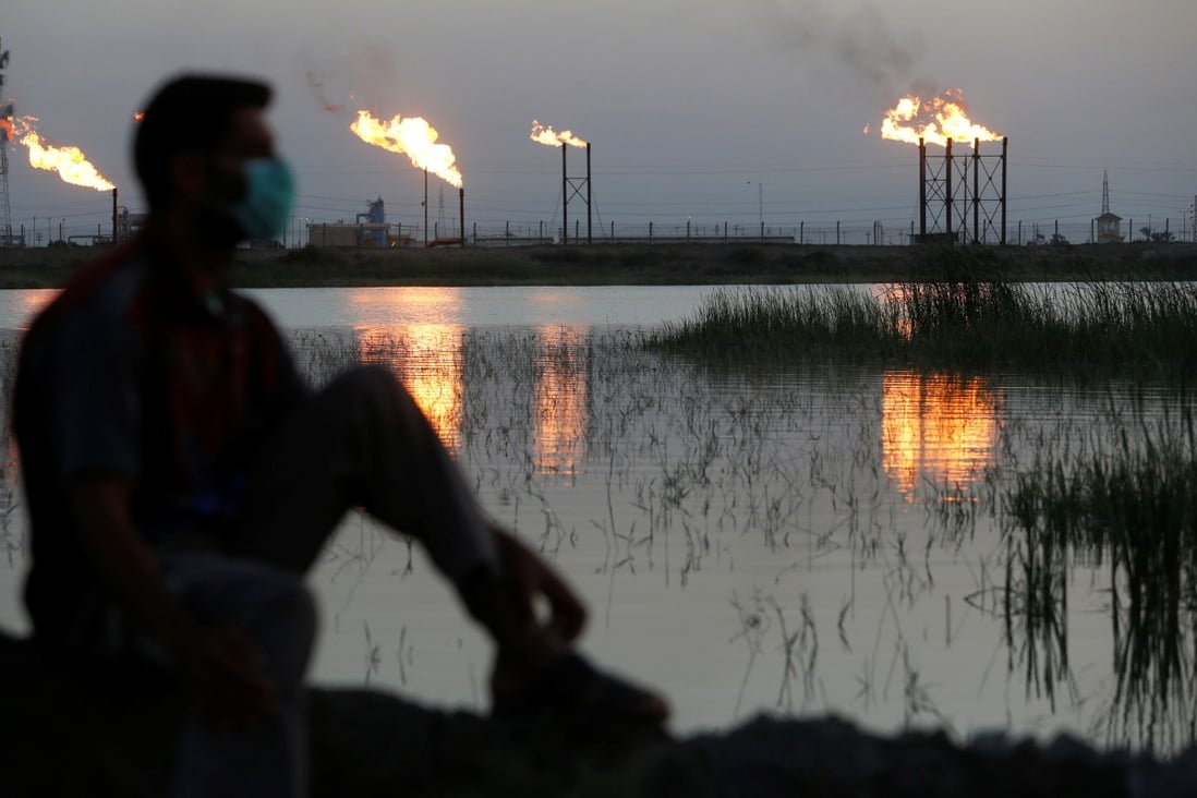 A man wearing a face mask is flanked by flare stacks at the Nahr Bin Umar oilfield, north of Basra, Iraq, on March 9, 2020. Photo: Reuters