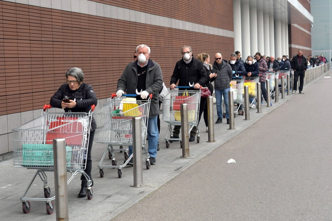 People wearing protective face masks lined up in front of a supermarket in Milan on March 12, 2020. Photo: EPA-EFE