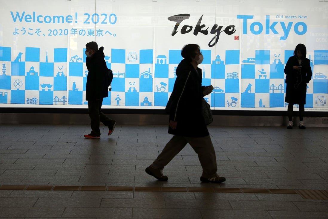People wearing protective masks walk by a billboard for the Tokyo 2020 Olympics near the Shinjuku station in Tokyo. Photo: Reuters