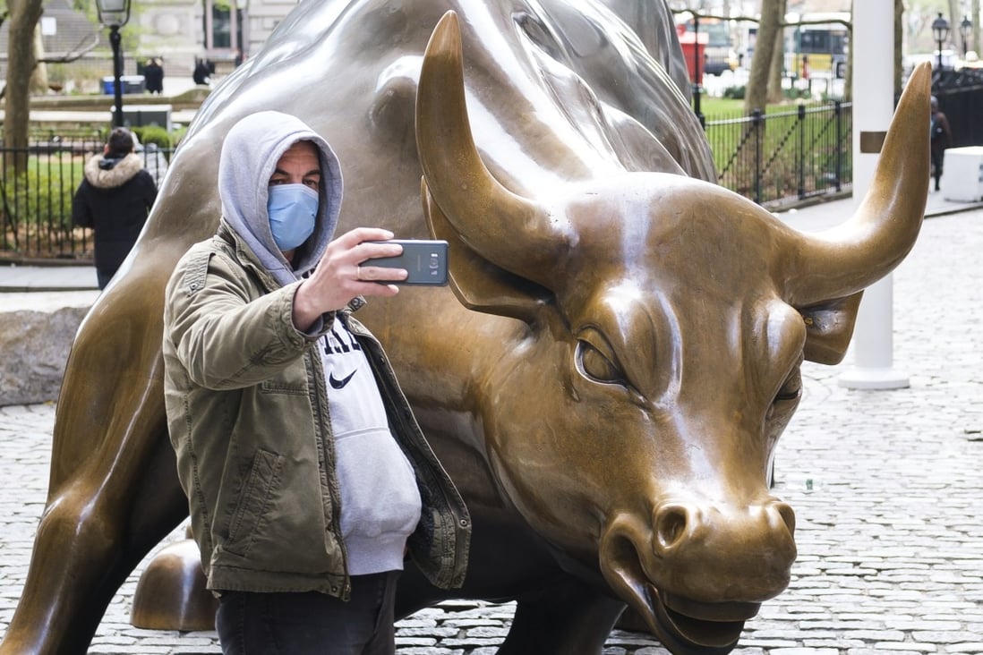 A man in a protective mask takes a selfie with the Charging Bull statue in New York. US markets rallied on Thursday after the Federal Reserve took steps to boost liquidity. Photo: EPA-EFE