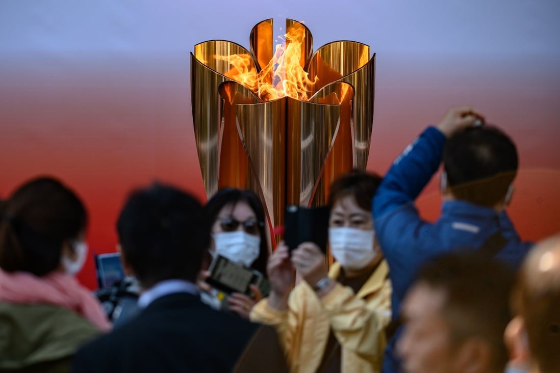 People wearing face masks take pictures in front of the Tokyo 2020 Olympic flame. Photo: AFP