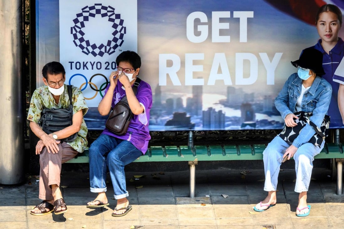 People wear face masks as a preventive measure against the spread of the coronavirus at a Bangkok bus stop in front of an advertisement for the Tokyo 2020 Olympics. Photo: AFP
