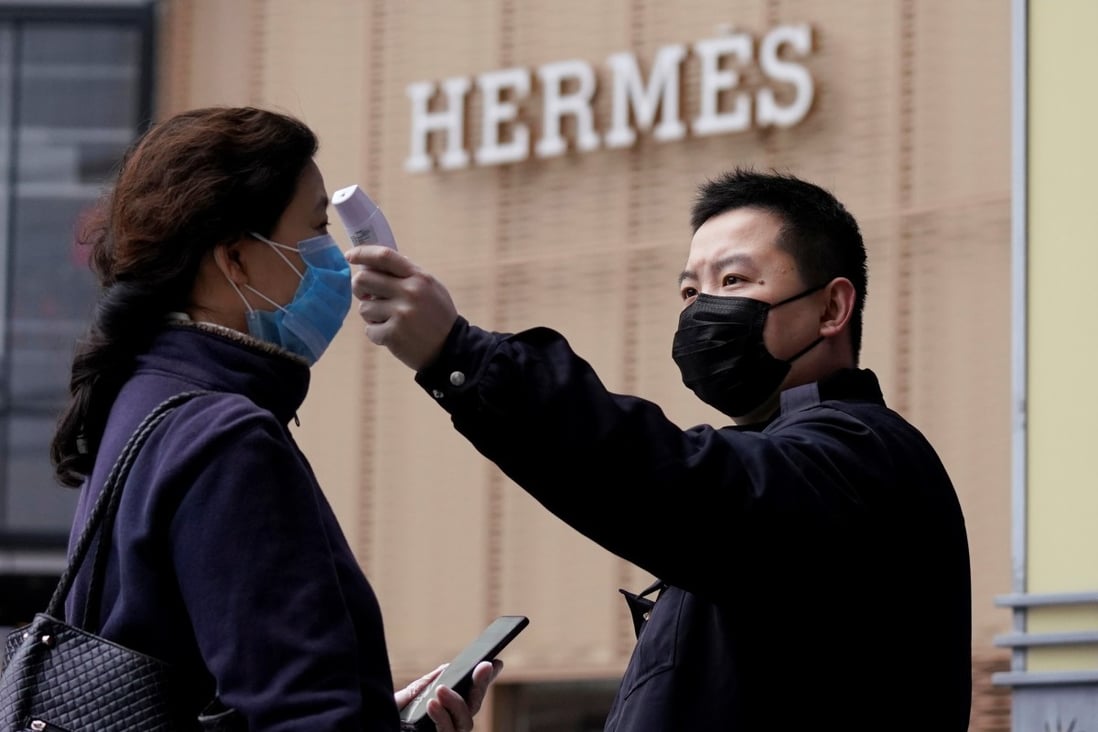 A management staff member measures the body temperature of a woman entering a shopping mall near a Hermès store in Wuhan, Hubei province, the epicentre of China’s coronavirus outbreak. Photo: Reuters