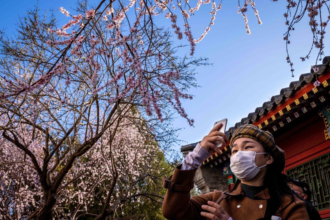 A woman wearing a face mask amid concerns over the spread of the novel coronavirus takes a photograph with her smartphone at a park in Beijing on March 14, 2020. Photo: AFP
