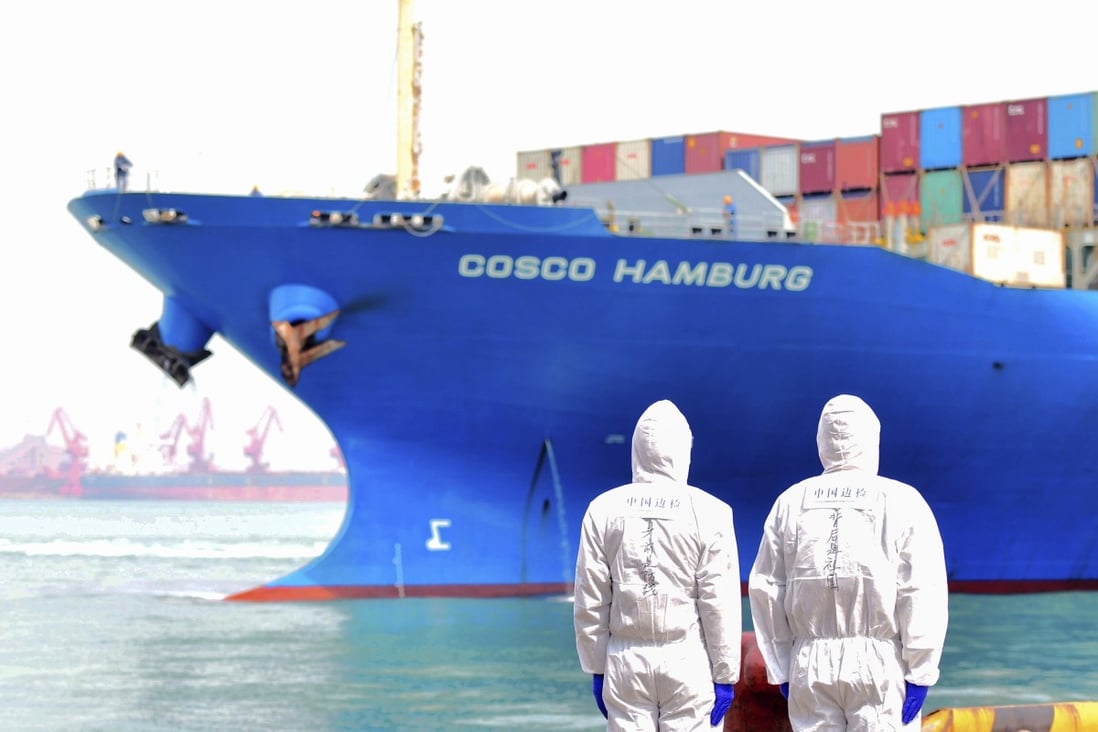 Workers in protective suits watch a container ship docked in Qingdao in eastern China's Shandong province. Photo: AP