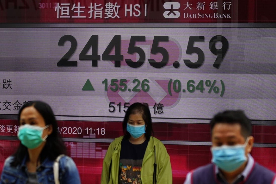 People wearing face masks walk past a bank electronic board showing the Hong Kong share index at Hong Kong Stock Exchange Tuesday, April 14, 2020. Asian shares rose Tuesday although investors were braced for a sobering first look at how the coronavirus pandemic has hurt global corporate earnings and the Chinese economy, the driver of growth for the region. (AP Photo/Vincent Yu)