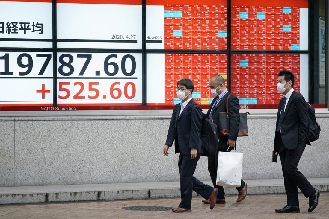 Pedestrians walk by a stock market indicator board in Tokyo on April 27, 2020. Photo: EPA-EFE