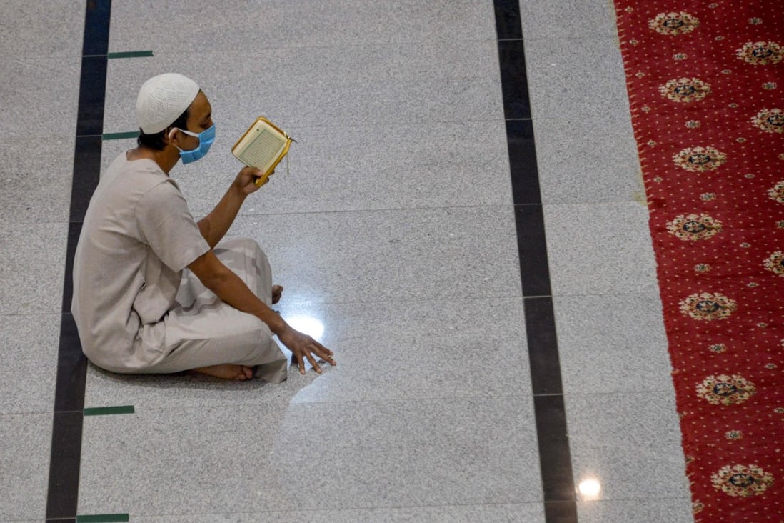 A man wearing a face mask and sitting far from anybody else reads the Koran after Friday prayers at the Al Makmur mosque in Banda Aceh, one of few mosques that were open. Photo: AFP