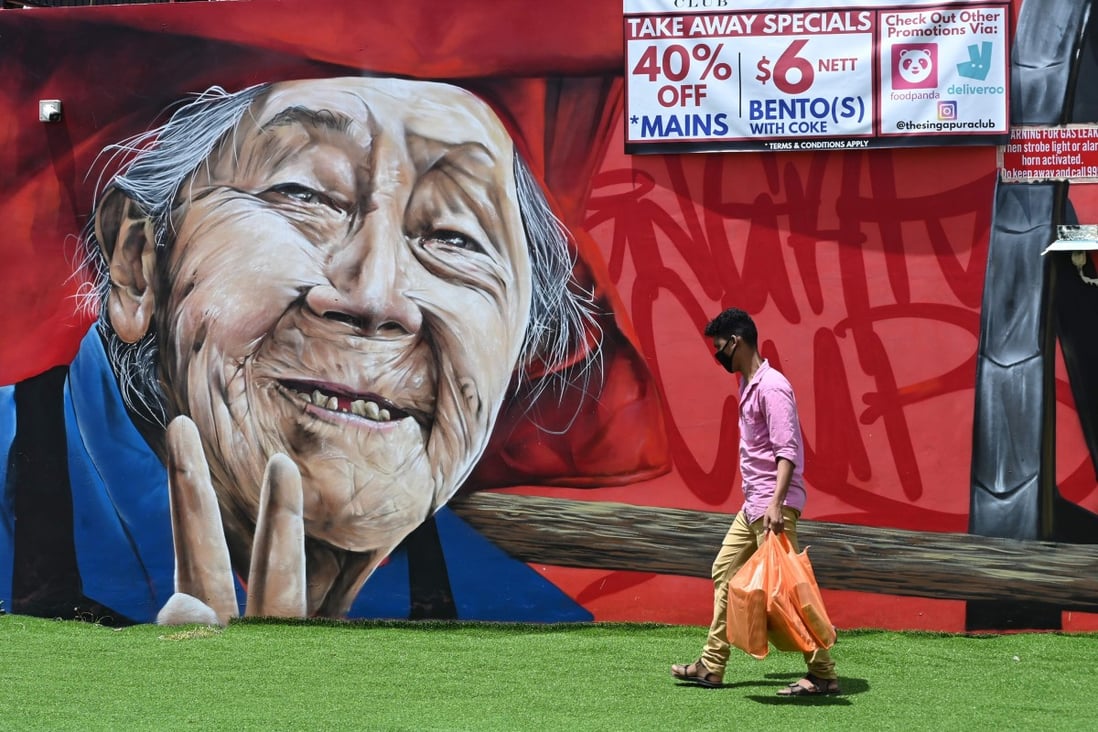A man wearing a protective face mask walks past a wall mural of an elderly person in Singapore. Photo: AFP