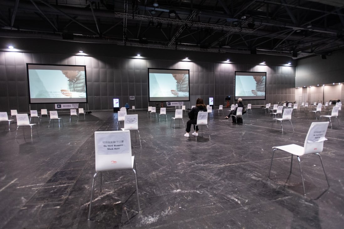 Travellers sit socially distanced while watching a video about saliva sampling in a coronavirus testing facility at the AsiaWorld-Expo in Hong Kong. Photo: Bloomberg