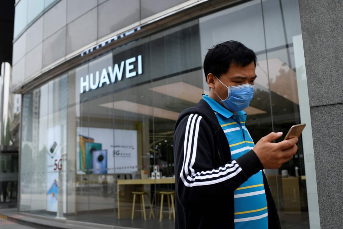 A man wearing a face mask uses his mobile phone as he walks past a Huawei store in Beijing on May 16, 2020. Photo: AFP