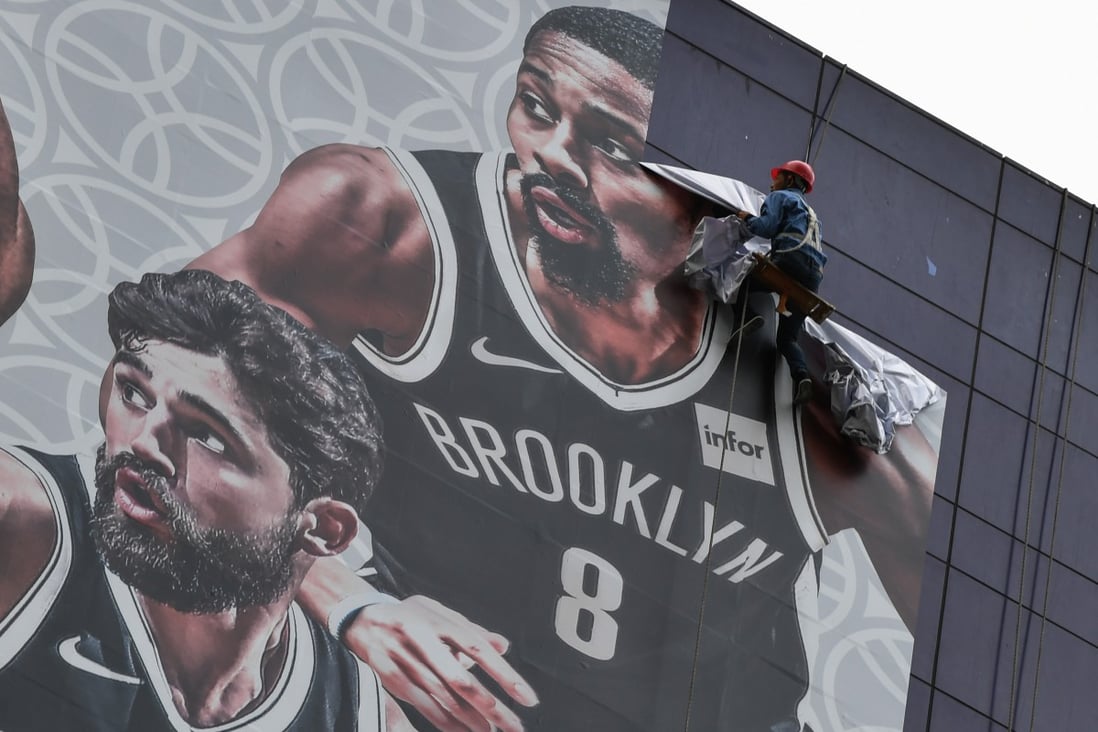 A worker removes a promotional banner for the NBA China Games in Shanghai in October, 2019. The preseason game between the Brooklyn Nets and the Los Angeles Lakers was played amid controversy. Photo: AFP